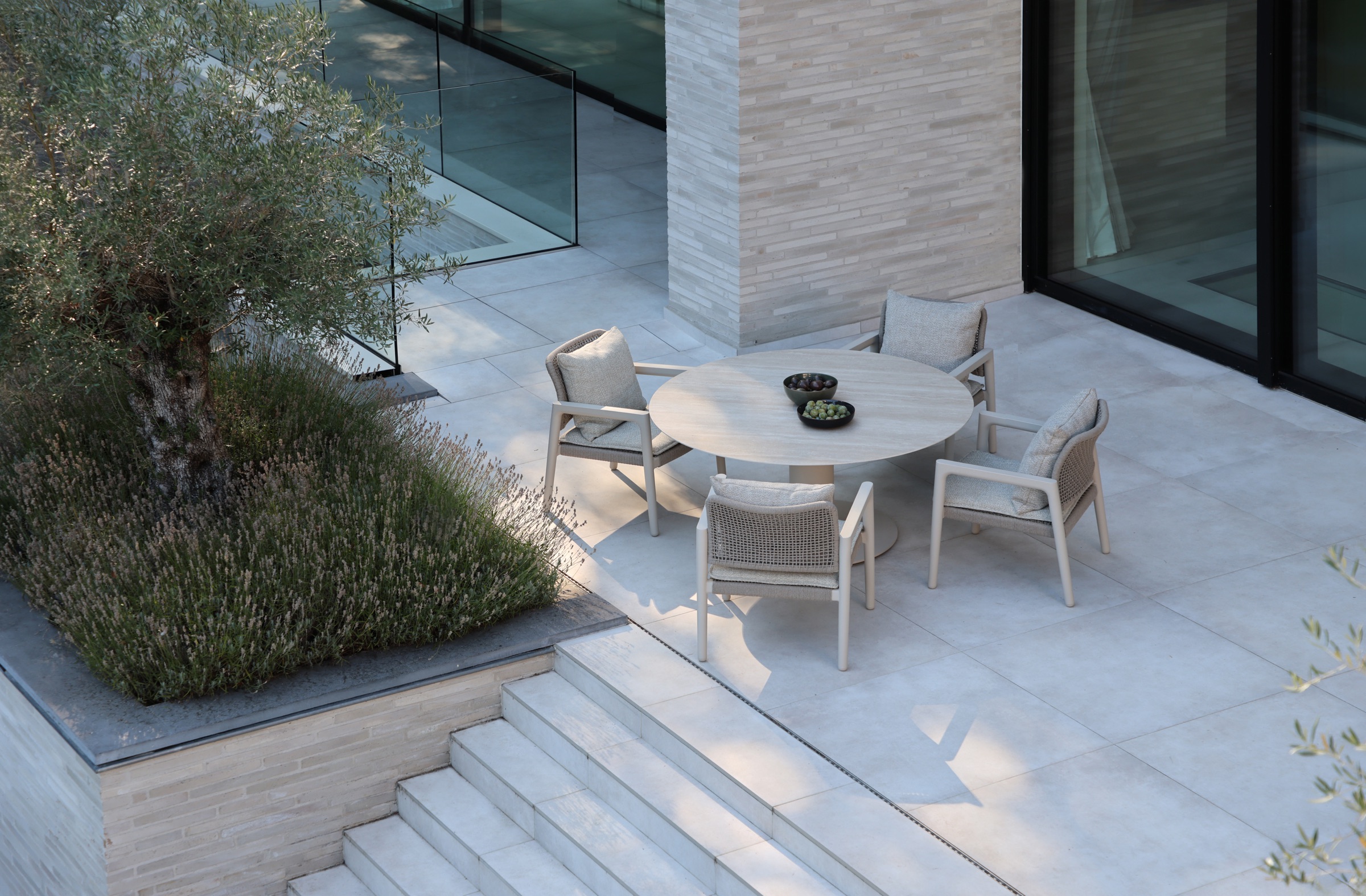 Round outdoor dining table with four rope armchairs on a stone terrace